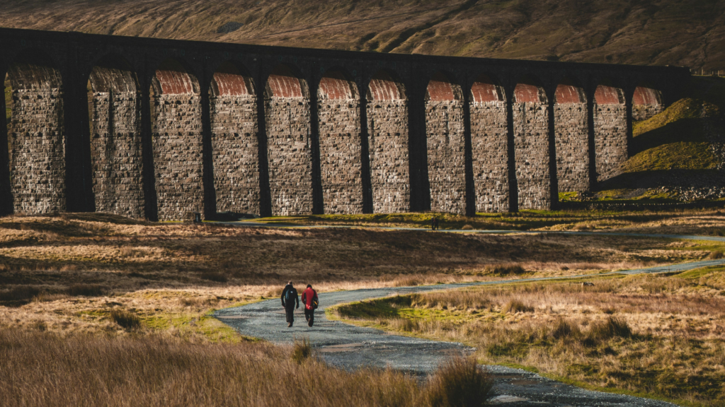 Two people walking towards the Ribblehead Viaduct, located at the base of Whernside, which is the highest of the Yorkshire Three Peaks.