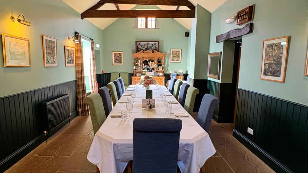 A long table set for a business meeting and private dining in a green-walled room with exposed wooden beams.