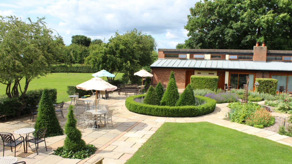 Landscaped pub garden at The Carpenters Arms in Felikirk, featuring paved seating areas with parasols and lush green lawns.